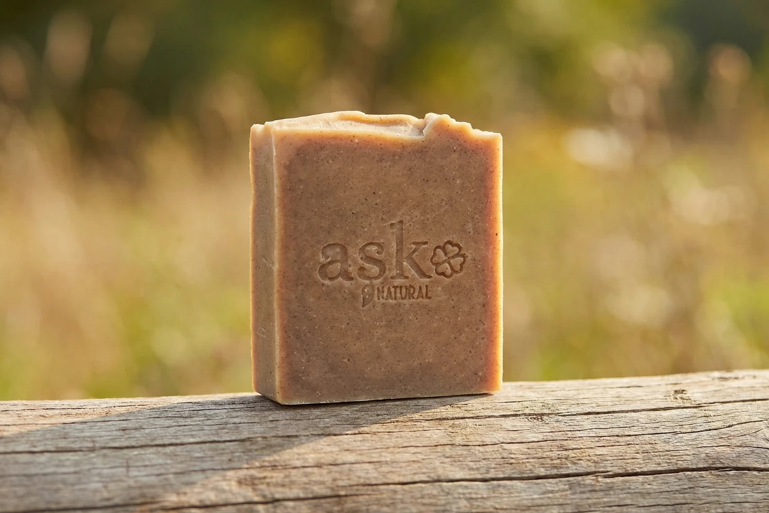 Handgemachte Argan Naturseife von ASK Natural - mit eingeprägtem Logo auf einem Holzstamm, vor natürlichem Hintergrund.