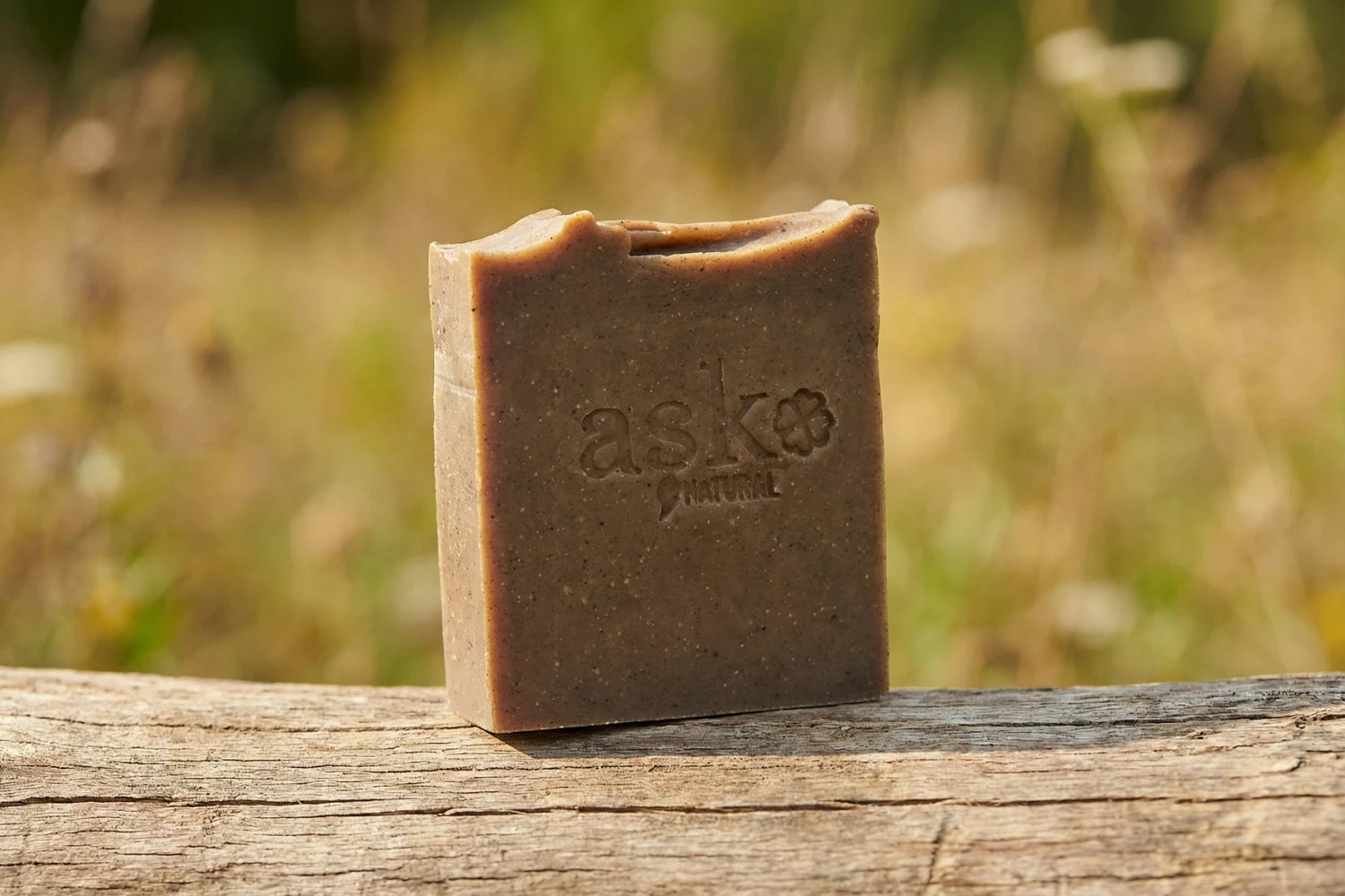Handgemachte Schwarzkümmelöl Naturseife von ASK Natural - mit eingeprägtem Logo auf einem Holzstamm, vor natürlichem Hintergrund.