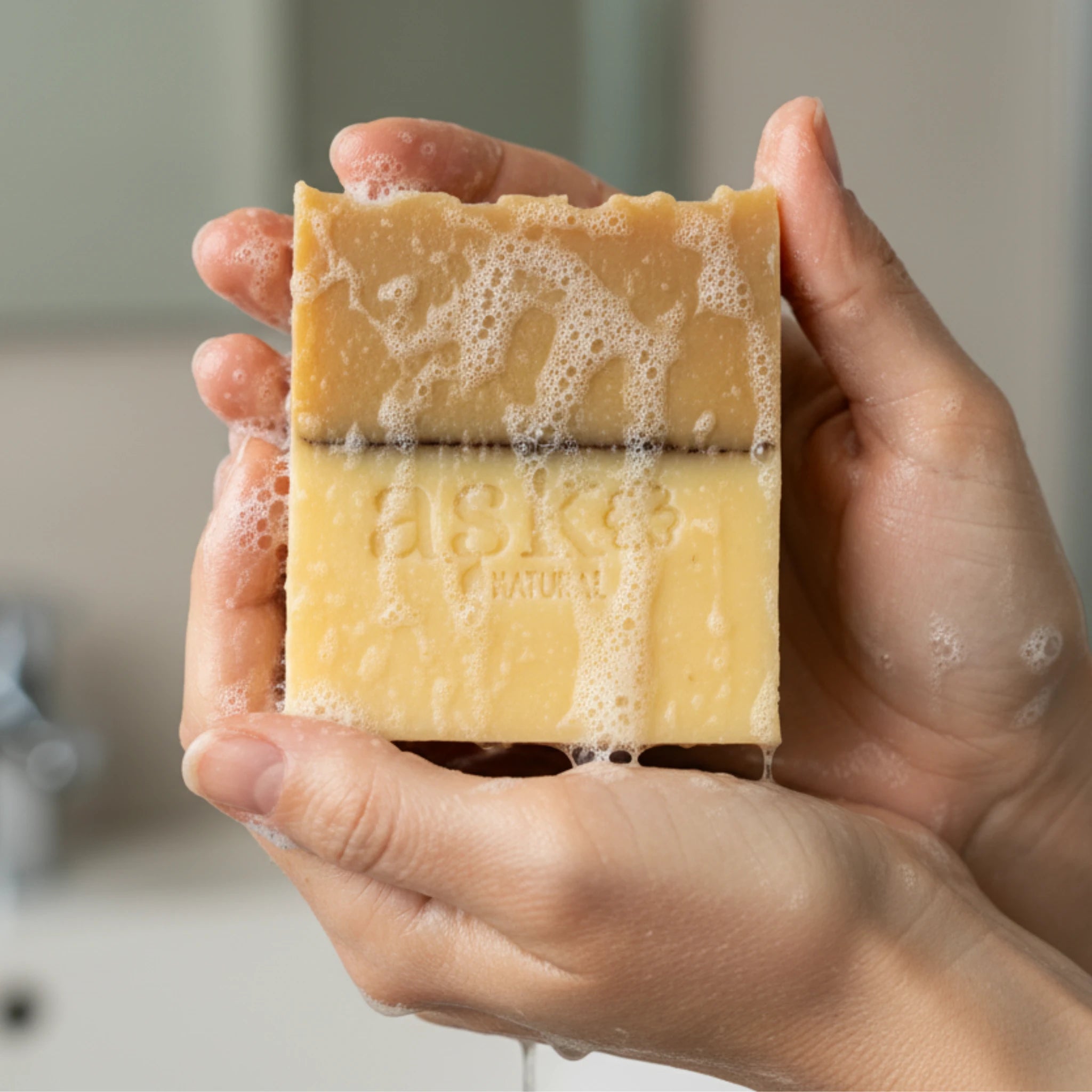 Nahaufnahme einer handgemachten Hafer Honig Seife von ASK Natural mit natürlicher Textur und cremigem Schaum in den Händen, hergestellt im traditionellen Kaltverfahren.