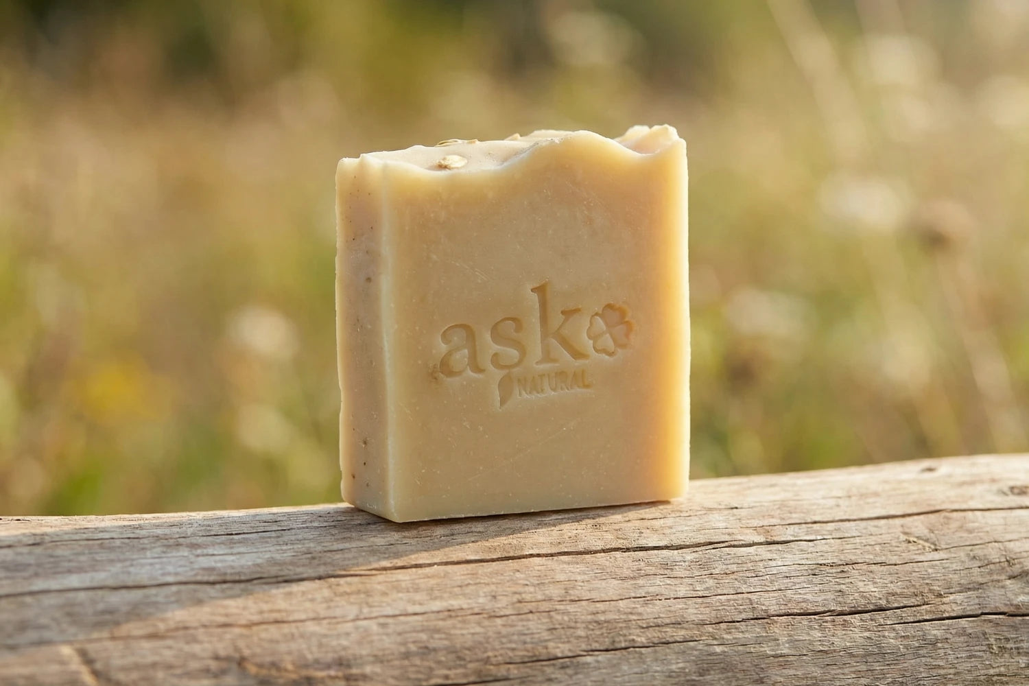Handgemachte Eselsmilch Naturseife von ASK Natural - mit eingeprägtem Logo auf einem Holzstamm, vor natürlichem Hintergrund.