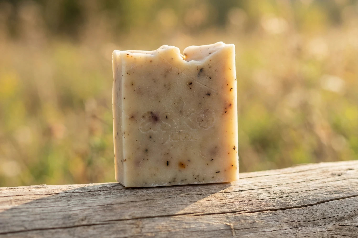 Handgemachte Johanniskrautöl Naturseife von ASK Natural - mit eingeprägtem Logo auf einem Holzstamm, vor natürlichem Hintergrund.