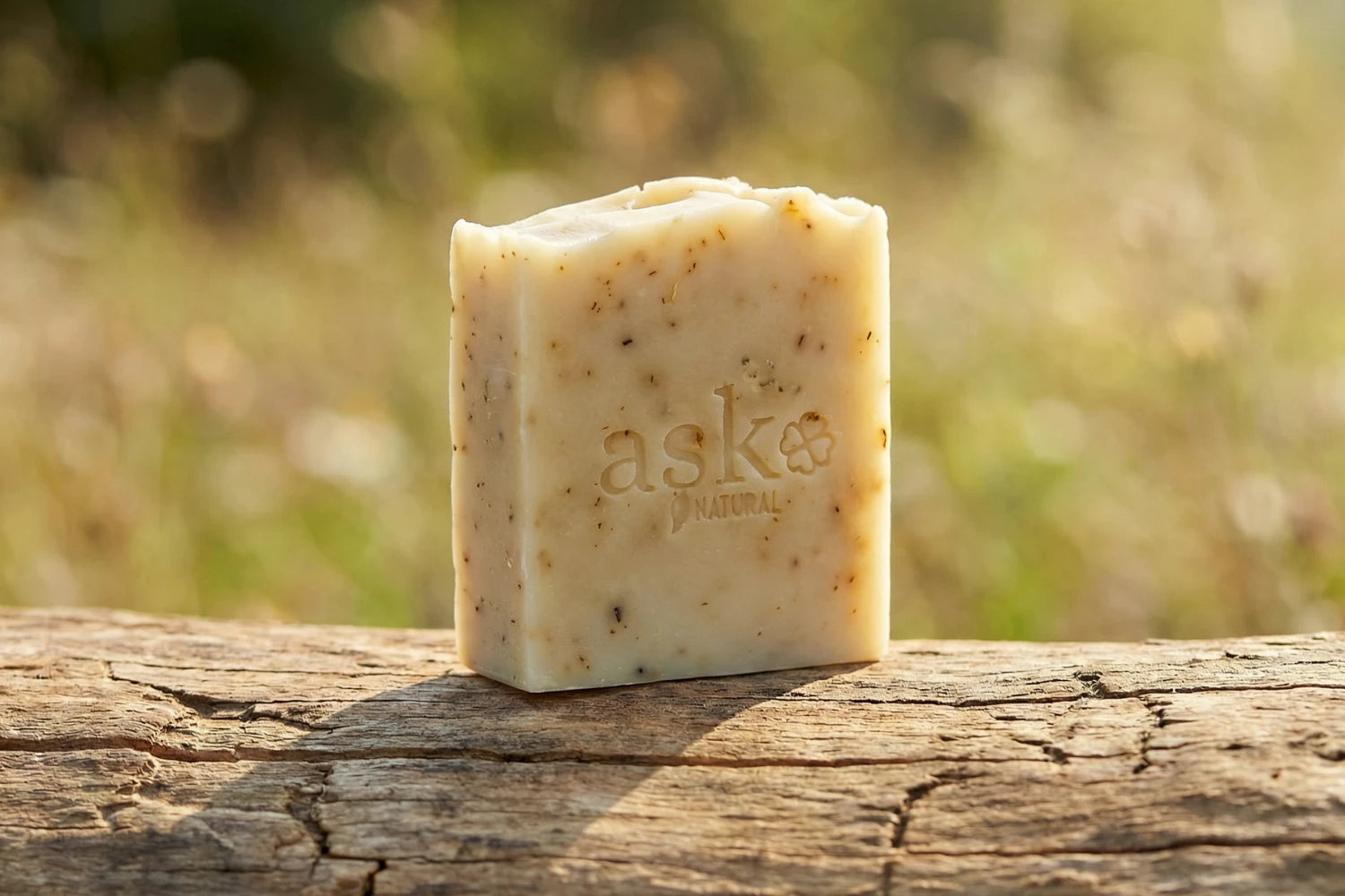 Handgemachte Rose Naturseife von ASK Natural - mit eingeprägtem Logo auf einem Holzstamm, vor natürlichem Hintergrund.