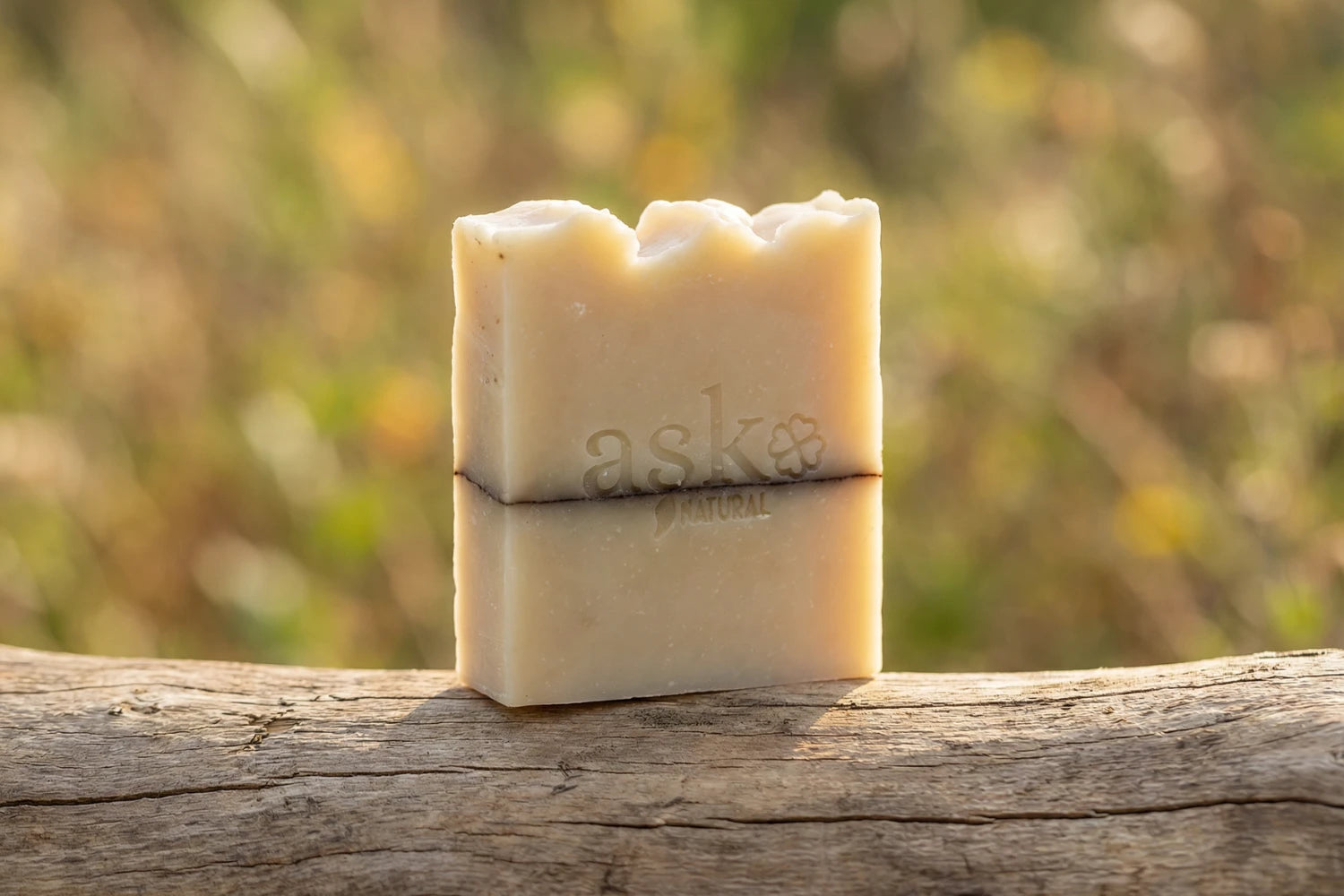 Handgemachte Sheabutter Naturseife von ASK Natural - mit eingeprägtem Logo auf einem Holzstamm, vor natürlichem Hintergrund.