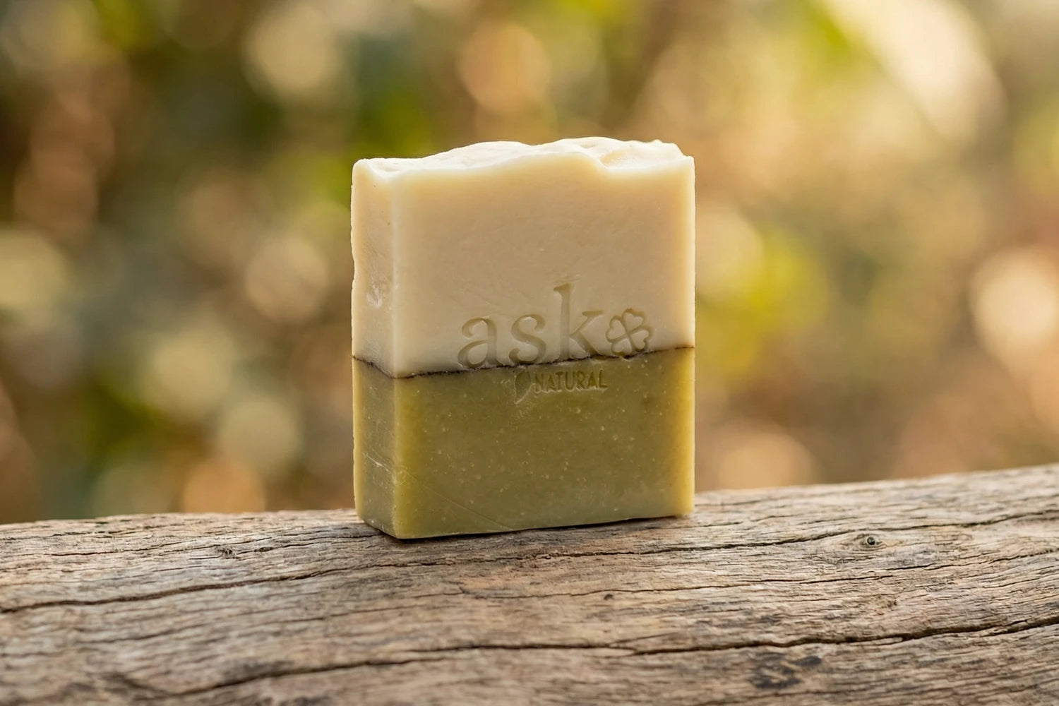 Handgemachte Teebaumöl Naturseife von ASK Natural - mit eingeprägtem Logo auf einem Holzstamm, vor natürlichem Hintergrund.