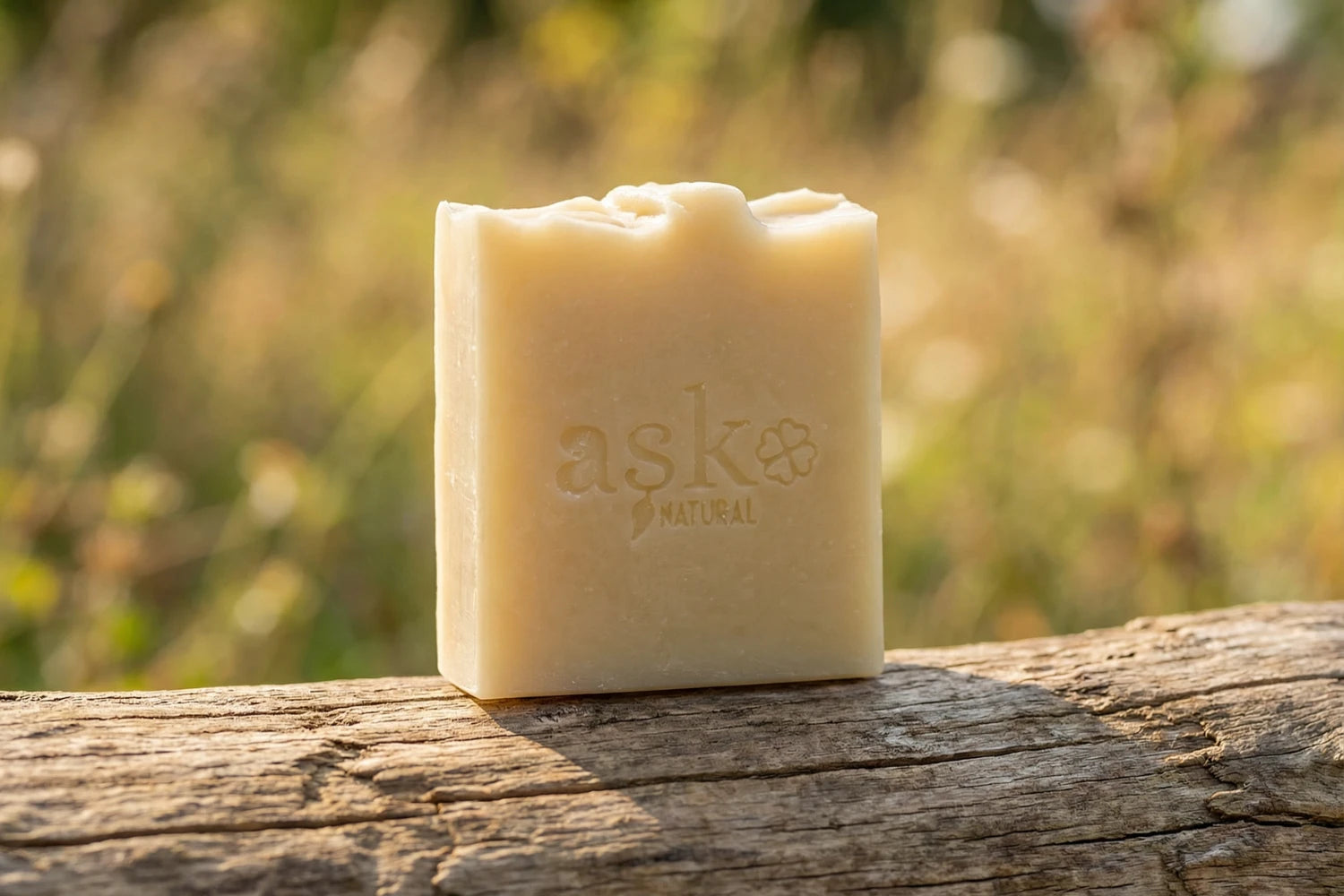 Handgemachte Ziegenmilch Naturseife von ASK Natural - mit eingeprägtem Logo auf einem Holzstamm, vor natürlichem Hintergrund.